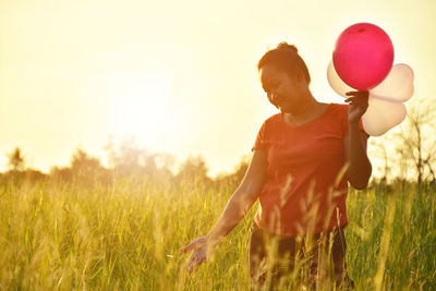 Woman holding balloons while standing on grassy field against sky