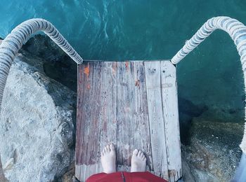 Low section of man standing on wooden ladder over sea