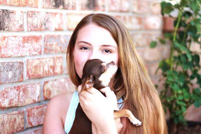 Portrait of young woman holding chihuahua puppy by brick wall