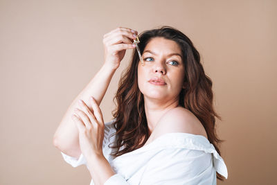 Beauty portrait of woman with pipette with oil on clean fresh skin face on beige background