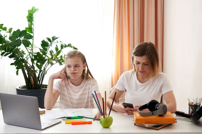 Mother and daughter sitting by desk at home