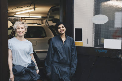 Portrait of smiling female mechanics standing at doorway of auto repair shop