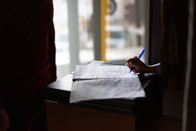 Cropped hand of female student writing in book at home