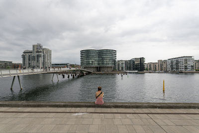 Rear view of woman on river by cityscape against sky