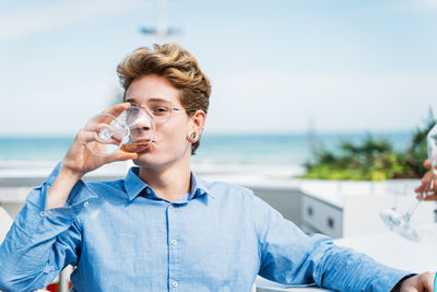 Portrait of man drinking water from glass against sea