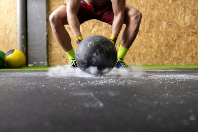 Powerful shirtless male throwing heavy ball against ground during fitness workout in gym