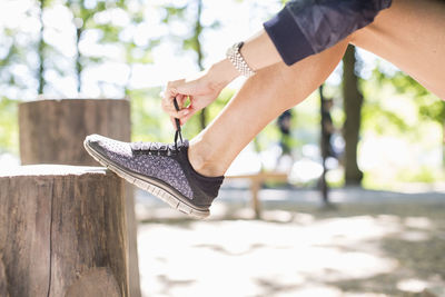 Low section of fit woman tying shoelace before jogging at park