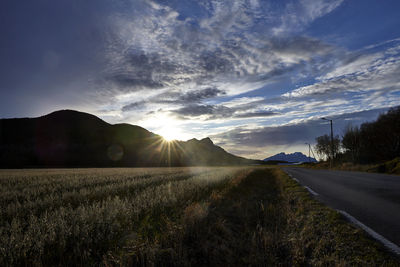 Road amidst field against sky during sunset