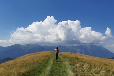 Rear view of woman walking mountain peak against cloudy sky