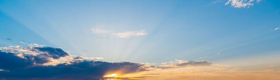 Low angle view of sunlight streaming through clouds during sunset