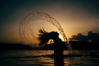 Silhouette woman standing on beach against sky during sunset