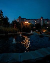 Illuminated buildings by lake against sky at night