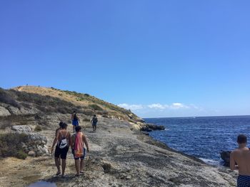 Rear view of men on sea shore against clear sky