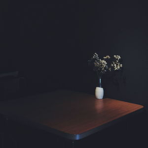 Flowers in vase on wooden table by wall at home