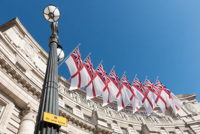 Low angle view of flags on buildings against clear blue sky