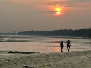 People walking on beach against sky during sunset