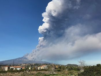 Buildings in city by smoke emitting from volcanic mountains against sky