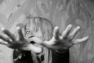 Portrait of woman with arms raised against wall