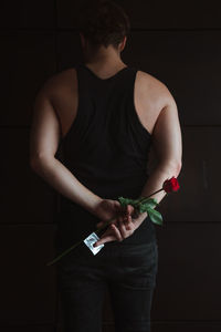 Rear view of man holding rose while standing against wall