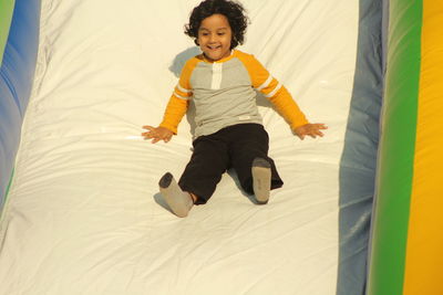 Cute smiling boy sliding on bouncy castle during sunny day