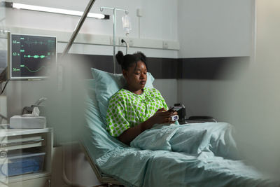 Side view of woman sitting on bed at home