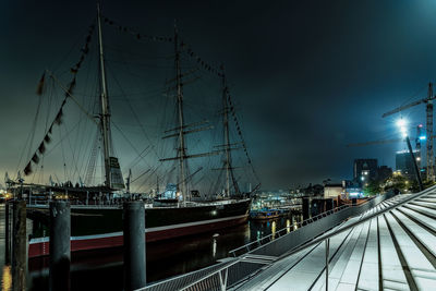 Sailboats moored at harbor against sky at night