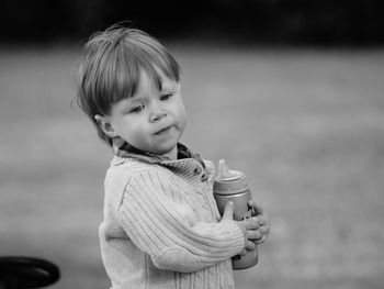 Cute boy holding milk bottle while standing outdoors