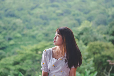 Young woman looking away while standing against blurred background