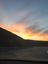 Road by mountains against sky during sunset