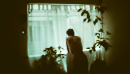 Rear view of silhouette woman standing against wall at home