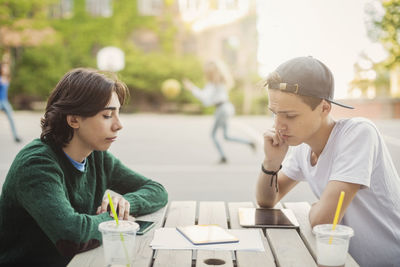 Teenagers using digital tablet at table outdoors