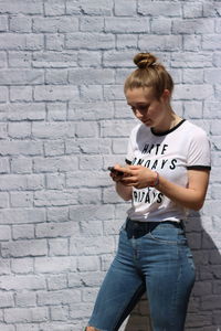 Teenage girl using mobile phone while standing against brick wall