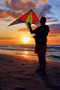 Silhouette man standing on beach against sky during sunset