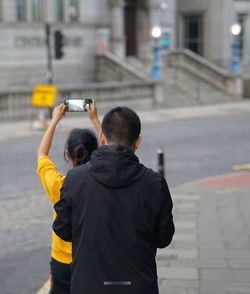 Rear view of man photographing at city street