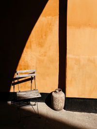 Chair and vase against wall in building on sunny day