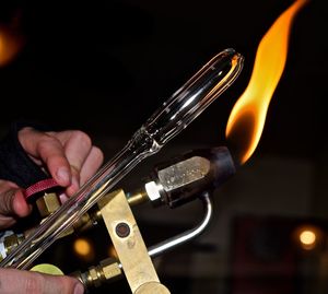 Cropped young woman holding flaming torch and glass in workshop