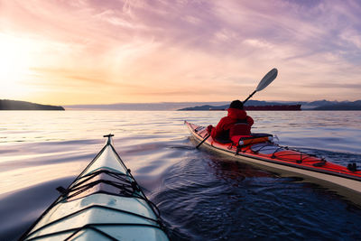 Man rowing boat in sea against sky during sunset