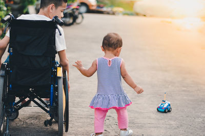 Rear view of brother on wheelchair with sister outdoors