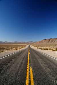 Empty road on desert against clear blue sky