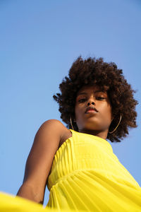 Low angle shot beautiful black woman with afro wearing yellow dress against blue sky