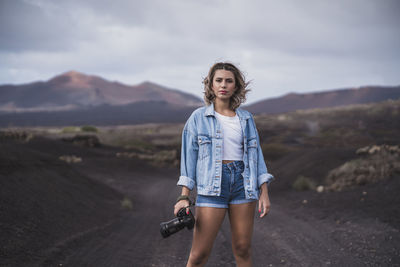 Young woman standing with camera on footpath at volcano el cuervo, lanzarote, spain