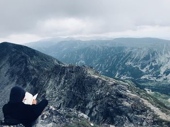 Rear view of man sitting on mountain against sky