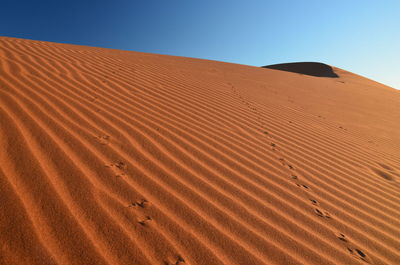 Low angle view of sand dune against clear blue sky