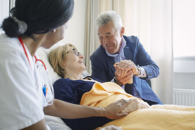 Senior man consoling female patient by doctor in hospital ward