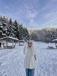 Portrait of young woman standing on snow covered field against sky