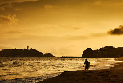 Silhouette man standing at beach against sky during sunset