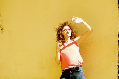 Young woman holding eye mask prop while standing against wall during sunny day