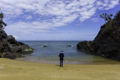 Rear view of woman on rock at beach against sky