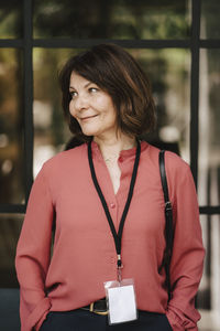 Smiling mature female professional standing with hands in pockets looking away