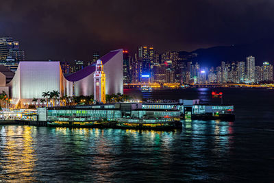 Illuminated city by river against sky at night